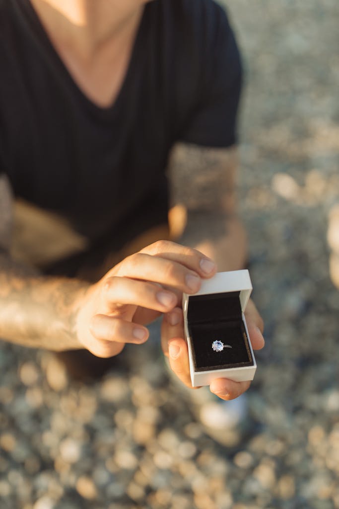 A man presents an engagement ring on a beach, creating a romantic proposal setting.