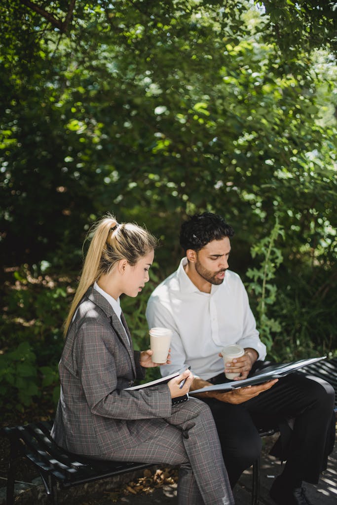 Two professionals engaged in a business discussion while enjoying coffee in a natural outdoor setting.