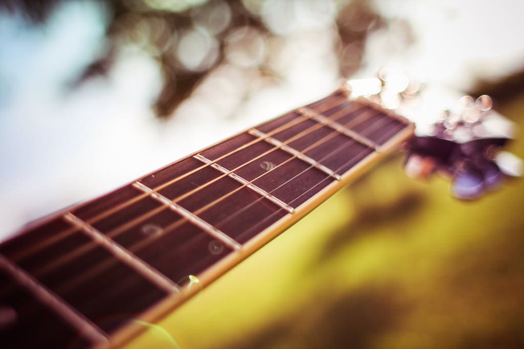 Focused close-up of a guitar neck with a blurred bokeh background, highlighting the strings.